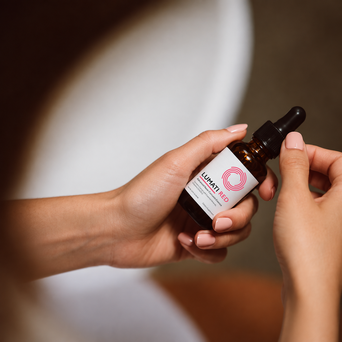 Hands holding an amber Lumati Red dropper bottle with a pink label against a soft neutral background.