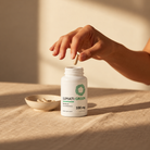 Hand reaching toward a Lumati Green 100 mg capsule bottle next to a small dish of capsules in soft sunlight.