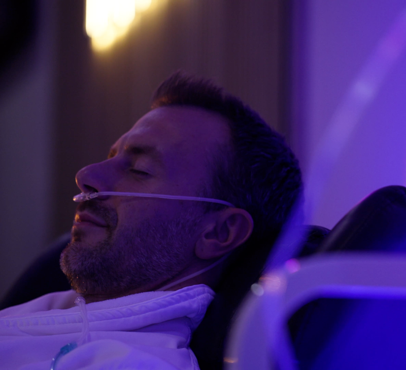 Man lying down with oxygen mask in a dimly lit room with purple lighting